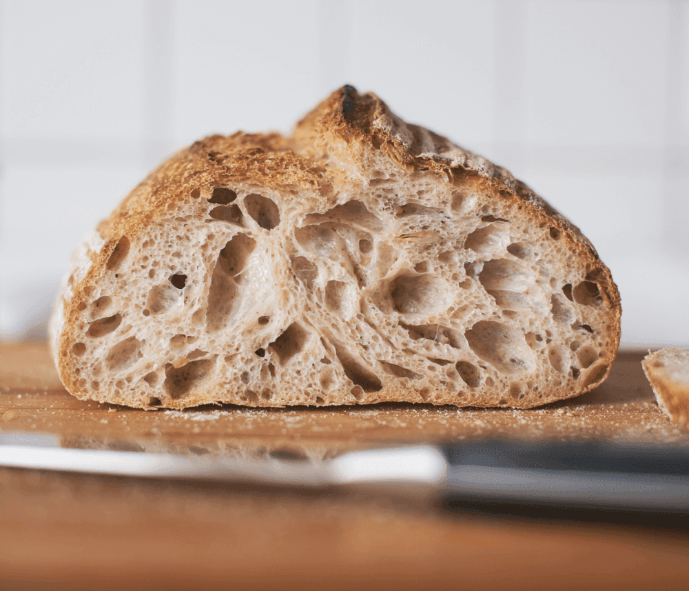 Close-up of a sliced sourdough bread loaf on a wooden cutting board, with a knife in the foreground. - Home Instead