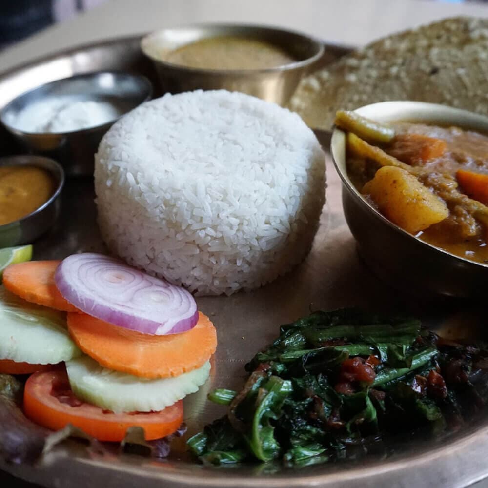 A traditional Indian meal on a metal plate with rice, vegetables, curry, roti, and various accompaniments. - Home Instead