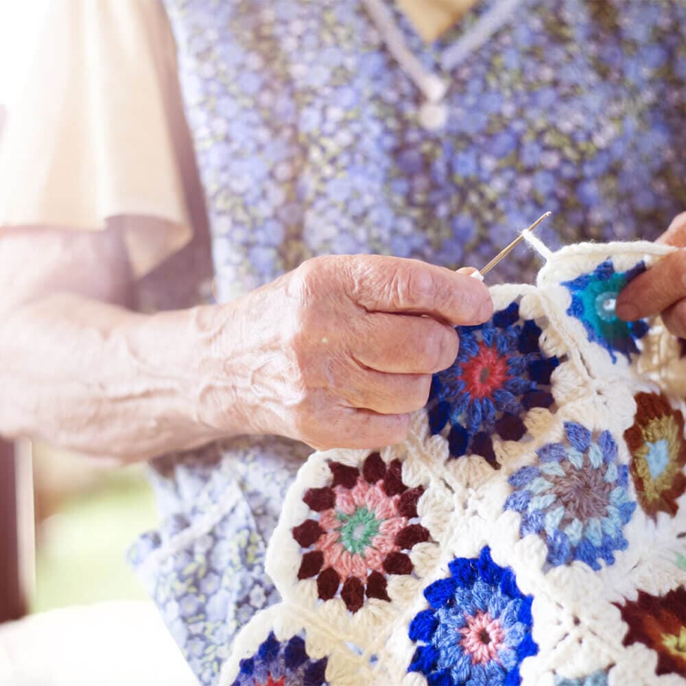 Elderly person hand crocheting a colorful patchwork blanket. - Home Instead