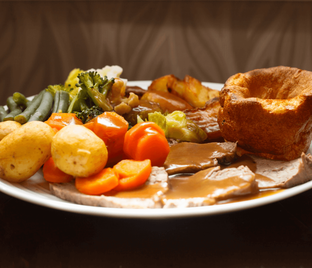 A plate of roast beef with vegetables, potatoes, and Yorkshire pudding, topped with gravy. - Home Instead
