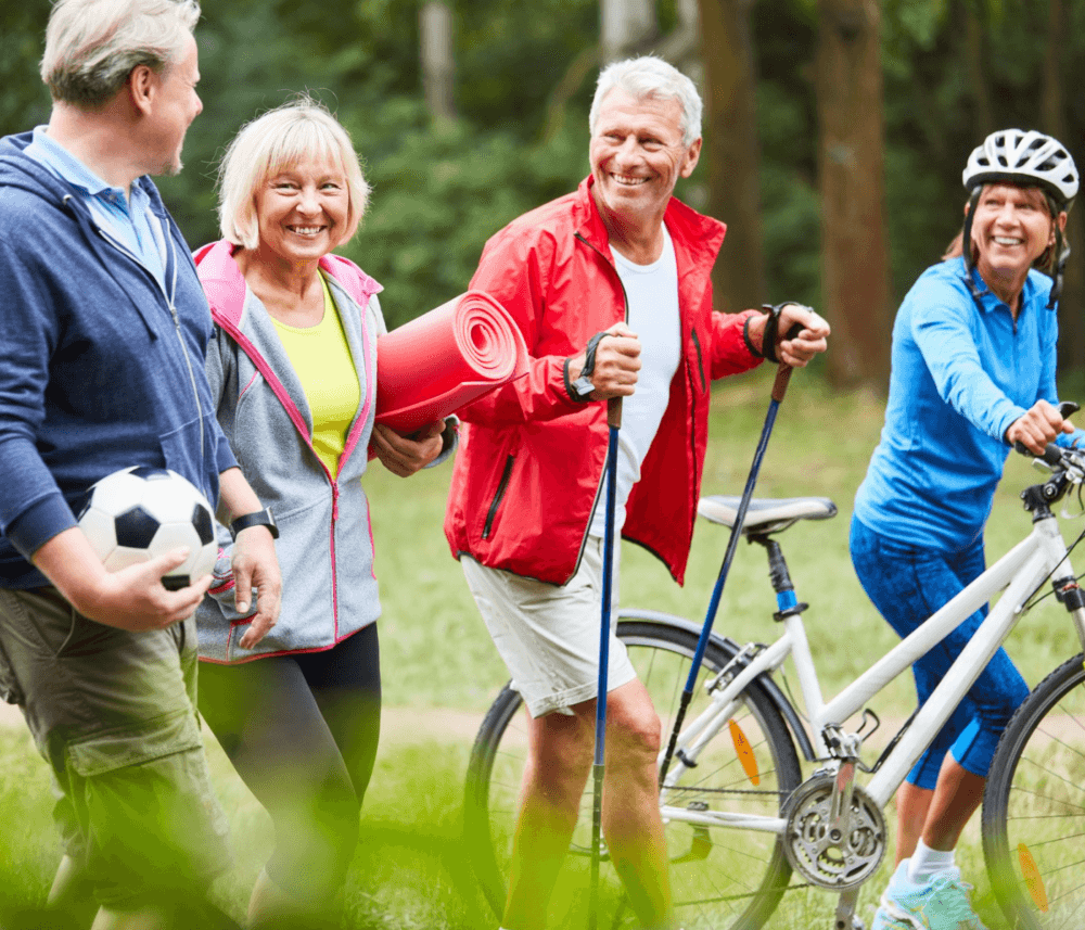 Four seniors enjoy outdoor activities together: walking with poles, carrying a yoga mat, holding a soccer ball, and biking. - Home Instead