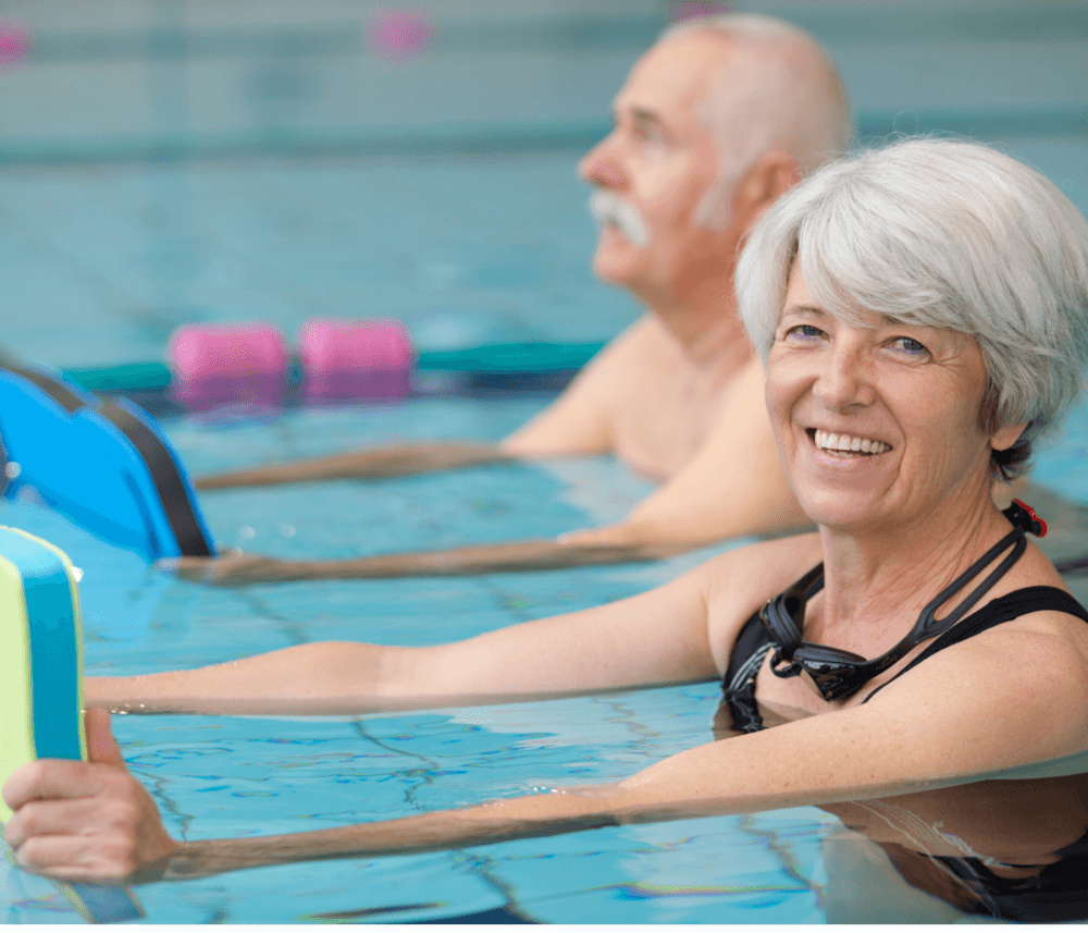 Older adults in a swimming pool holding kickboards, with one smiling woman in the foreground. - Home Instead