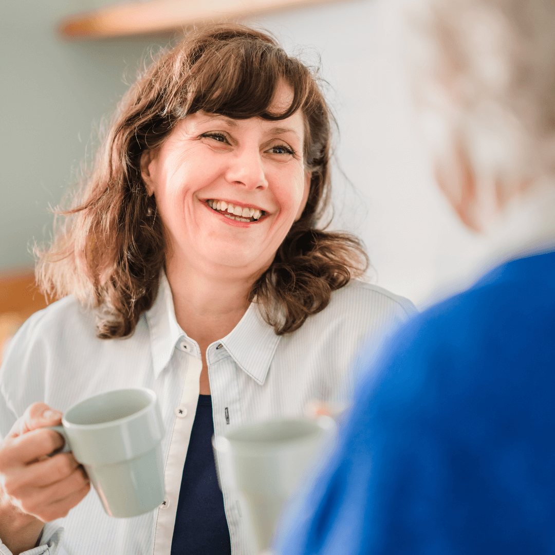 Care professional laughing with a client holding a hot drink