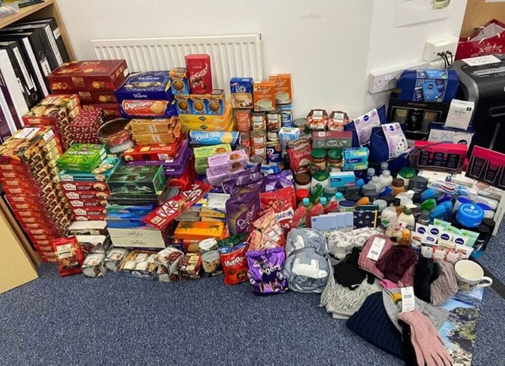 A large collection of assorted food items, toiletries, and clothing spread out on the floor in front of a radiator. - Home Instead