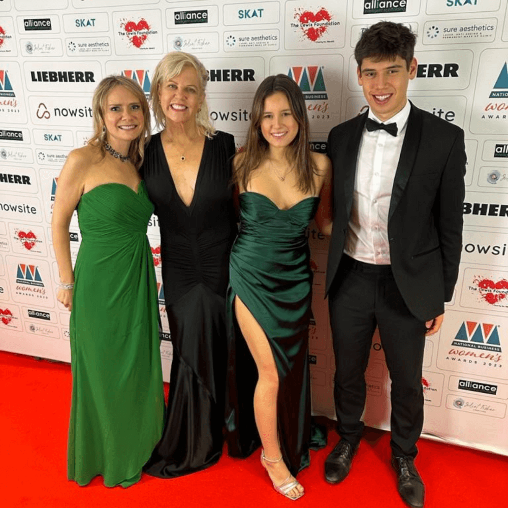 Four people in formal attire pose on a red carpet at a gala event, with a branded step-and-repeat backdrop behind them. - Home Instead