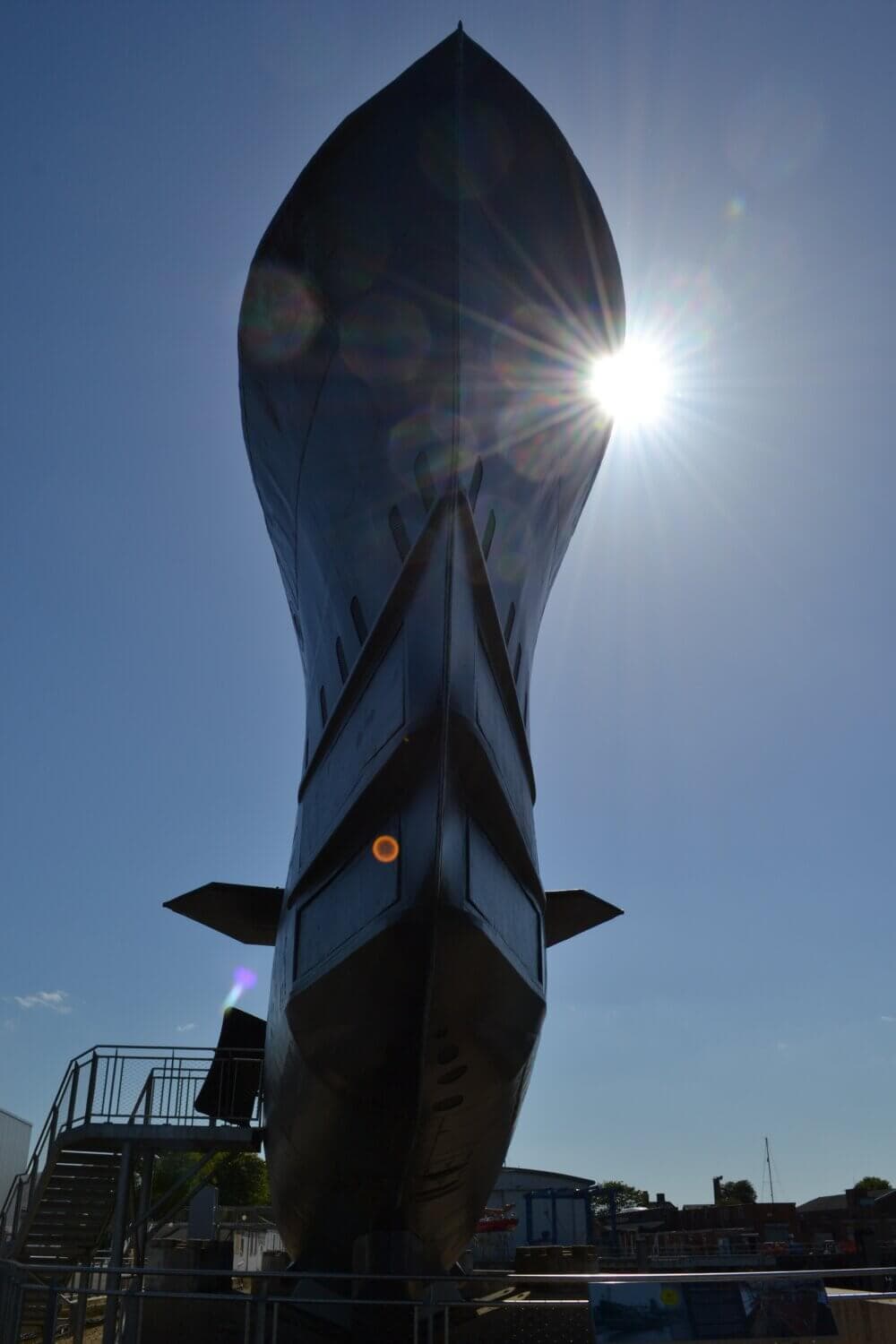 Sunlit view of a large ship's hull with the sun shining brightly behind it, casting a dramatic silhouette. - Home Instead