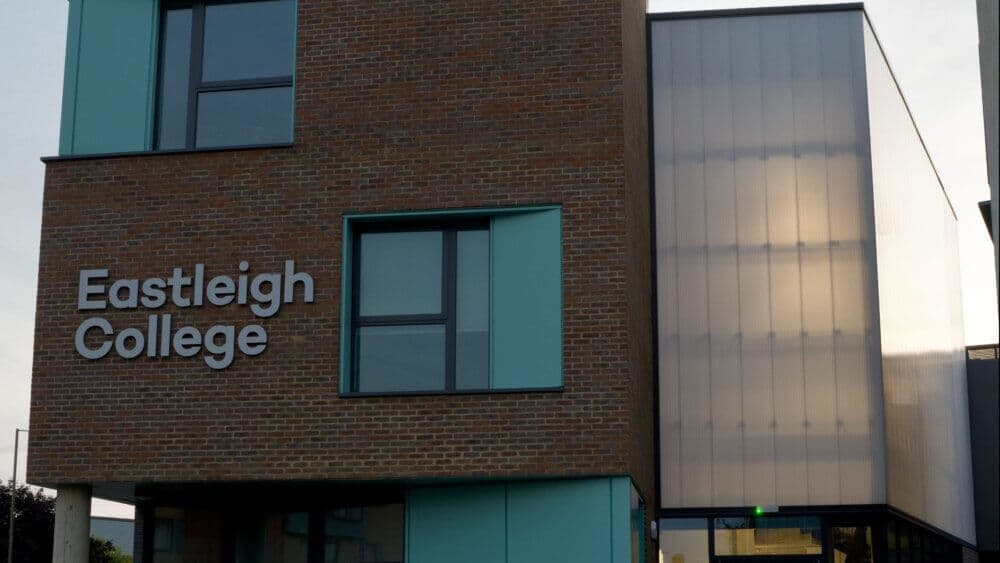 Exterior of a modern brick and glass building with a sign reading "Eastleigh College" on the side. - Home Instead