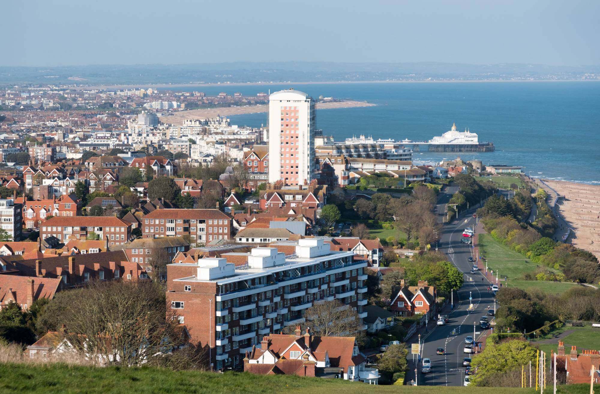 A coastal town with numerous buildings, a tall white tower, and a ferry on the ocean in the background. - Home Instead