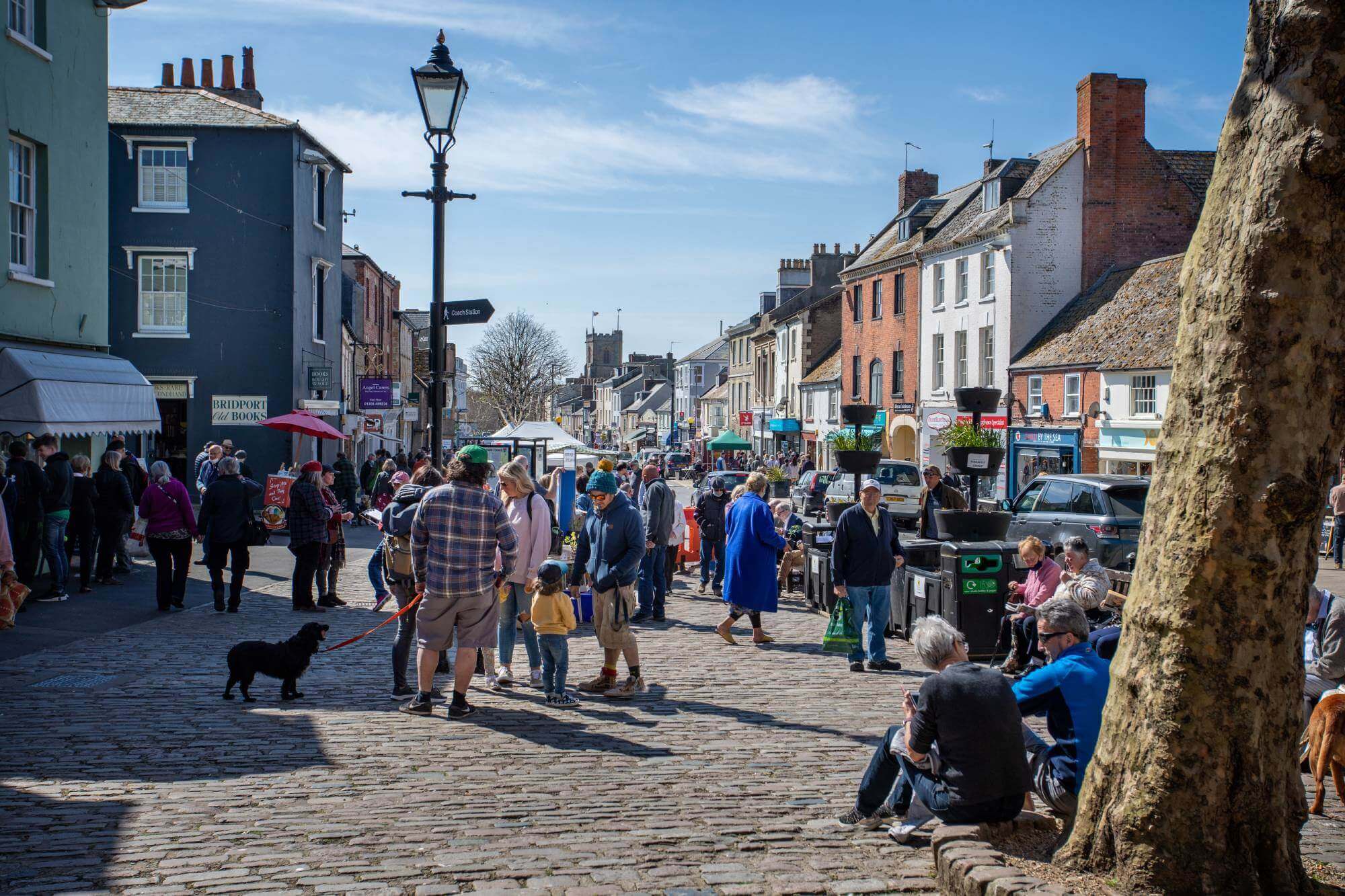 People walking and socializing in a vibrant outdoor market on a sunny day, with various shops and buildings in the background. - Home Instead