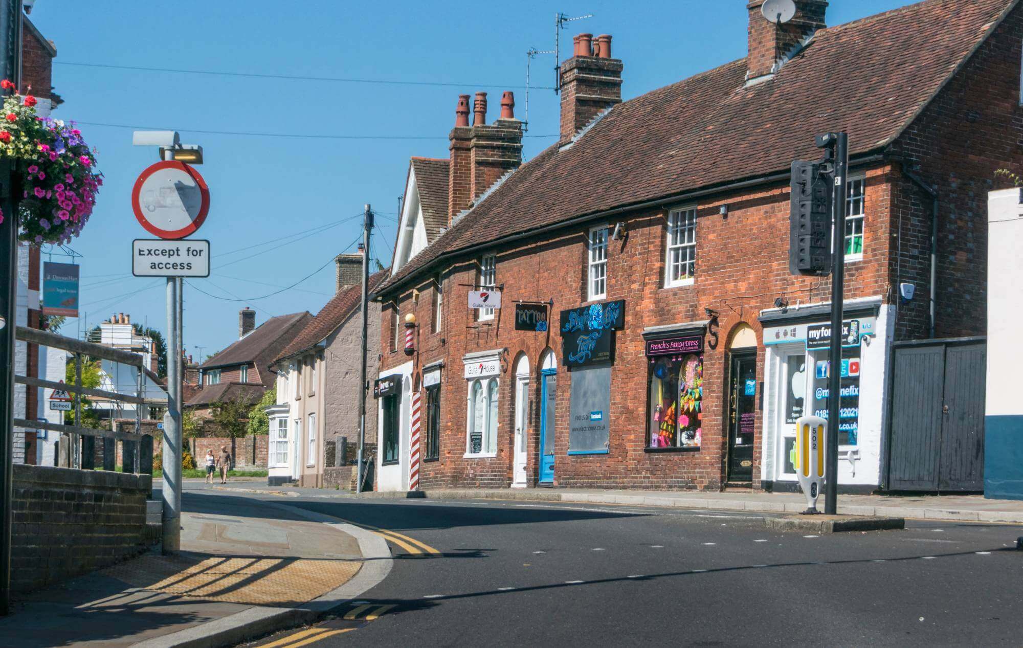 Street view of a quaint town with brick buildings, various shops, and a "no vehicles" sign on a sunny day. - Home Instead
