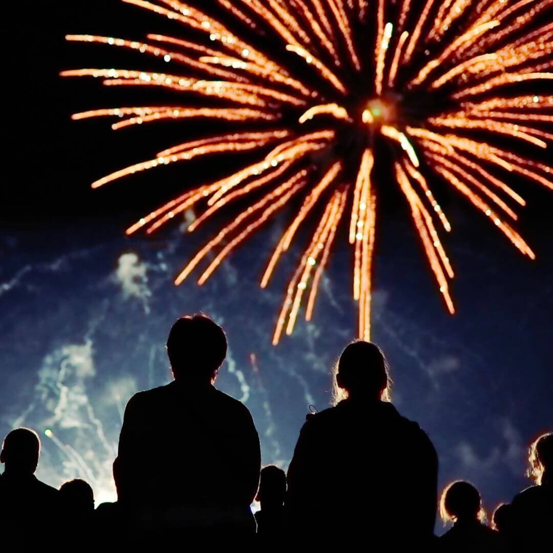 Silhouettes of people watching a vibrant fireworks display in the night sky. - Home Instead