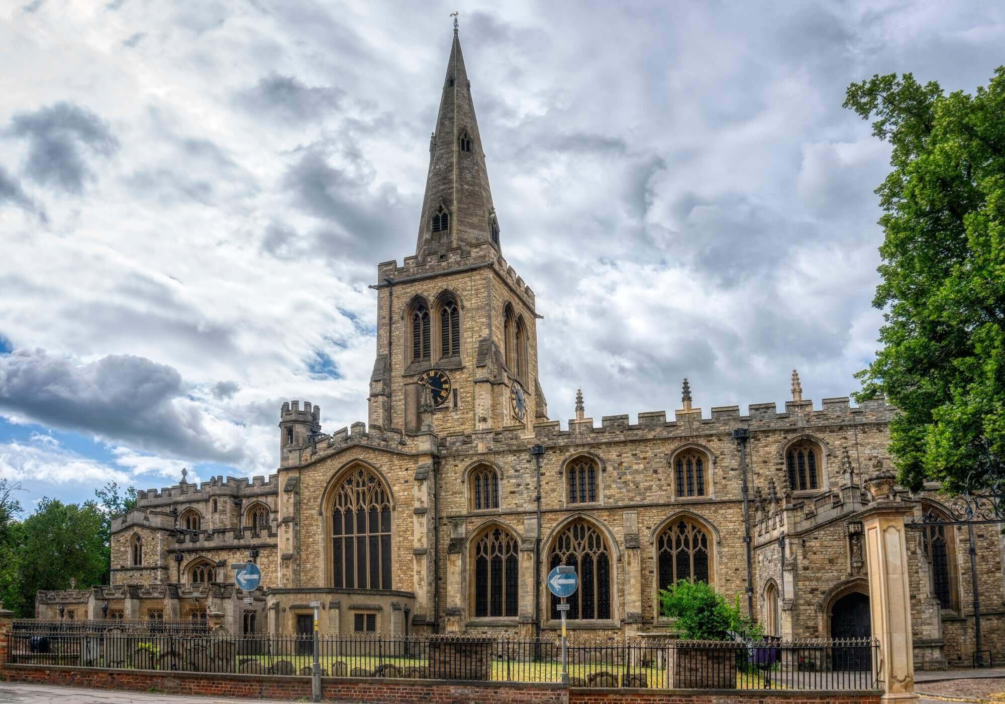 Historic stone church with tall spire, large arched windows, and cloudy sky, framed by trees on either side. - Home Instead