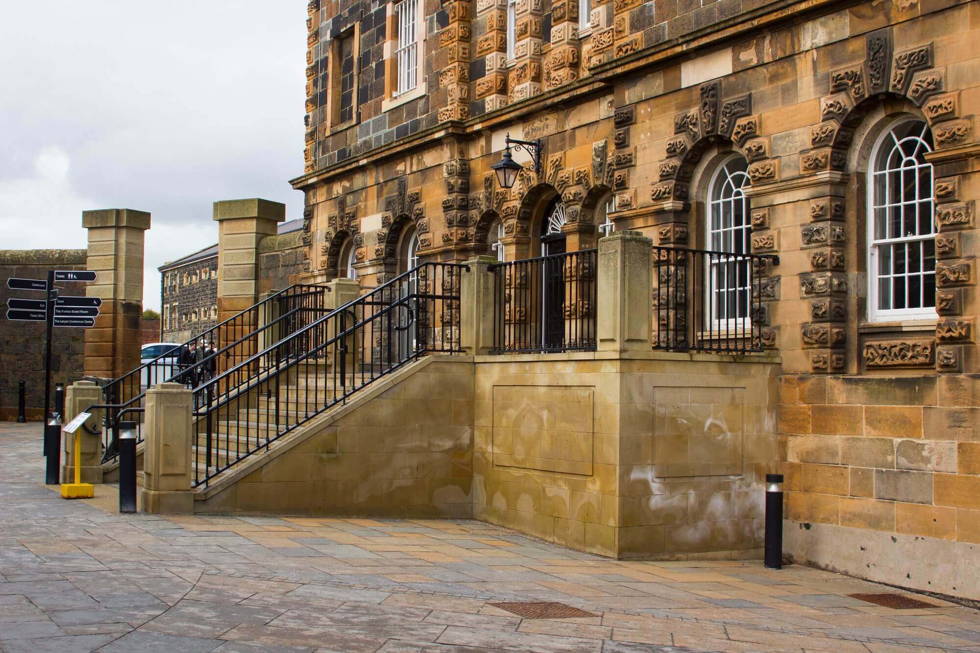Historic stone building with arched windows and a staircase leading to the entrance, next to a signpost. - Home Instead