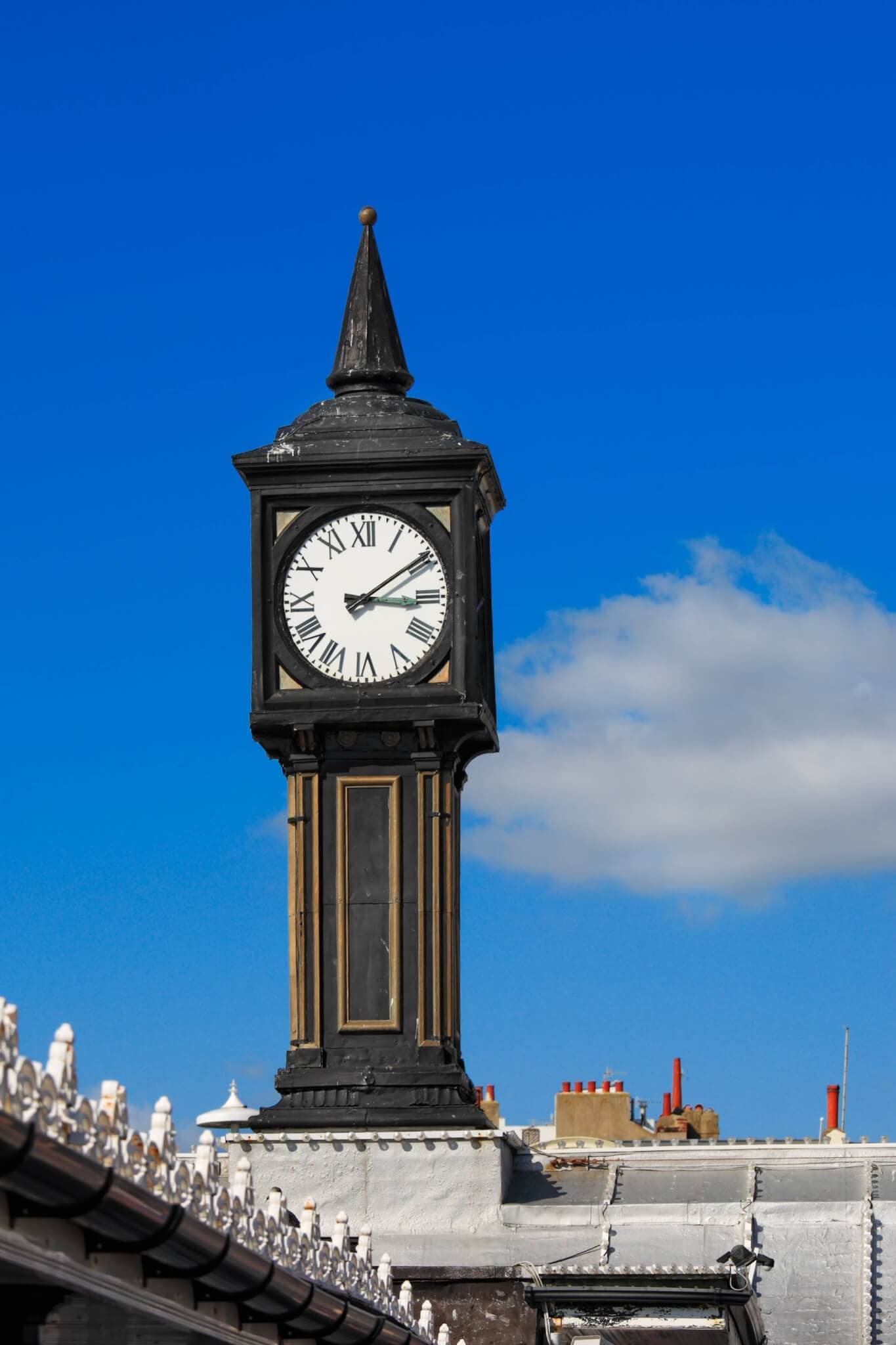 A classic black clock tower with Roman numerals against a bright blue sky and white clouds. - Home Instead