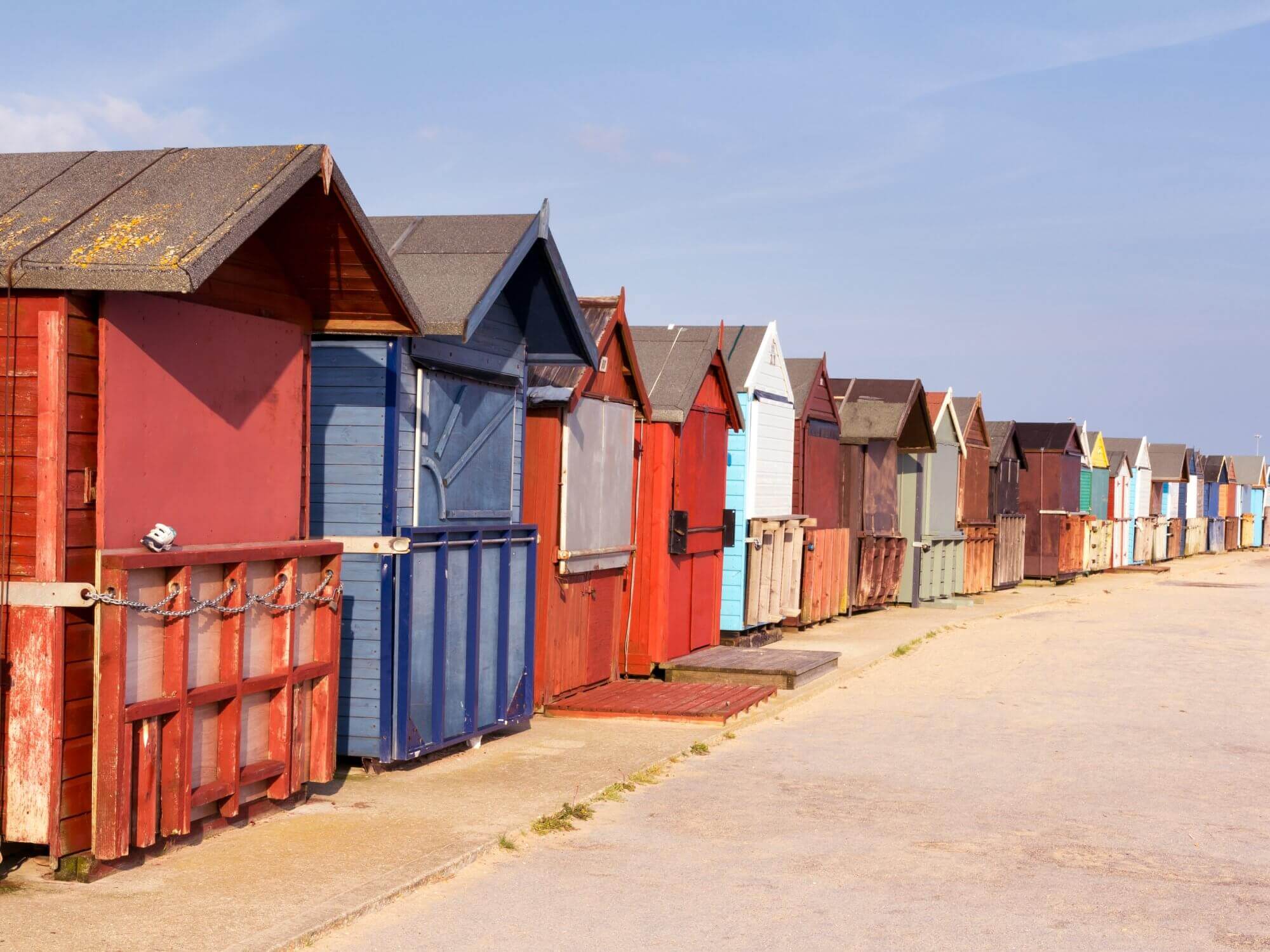 A row of colorful beach huts on a sunny day, with a clear sky in the background. - Home Instead