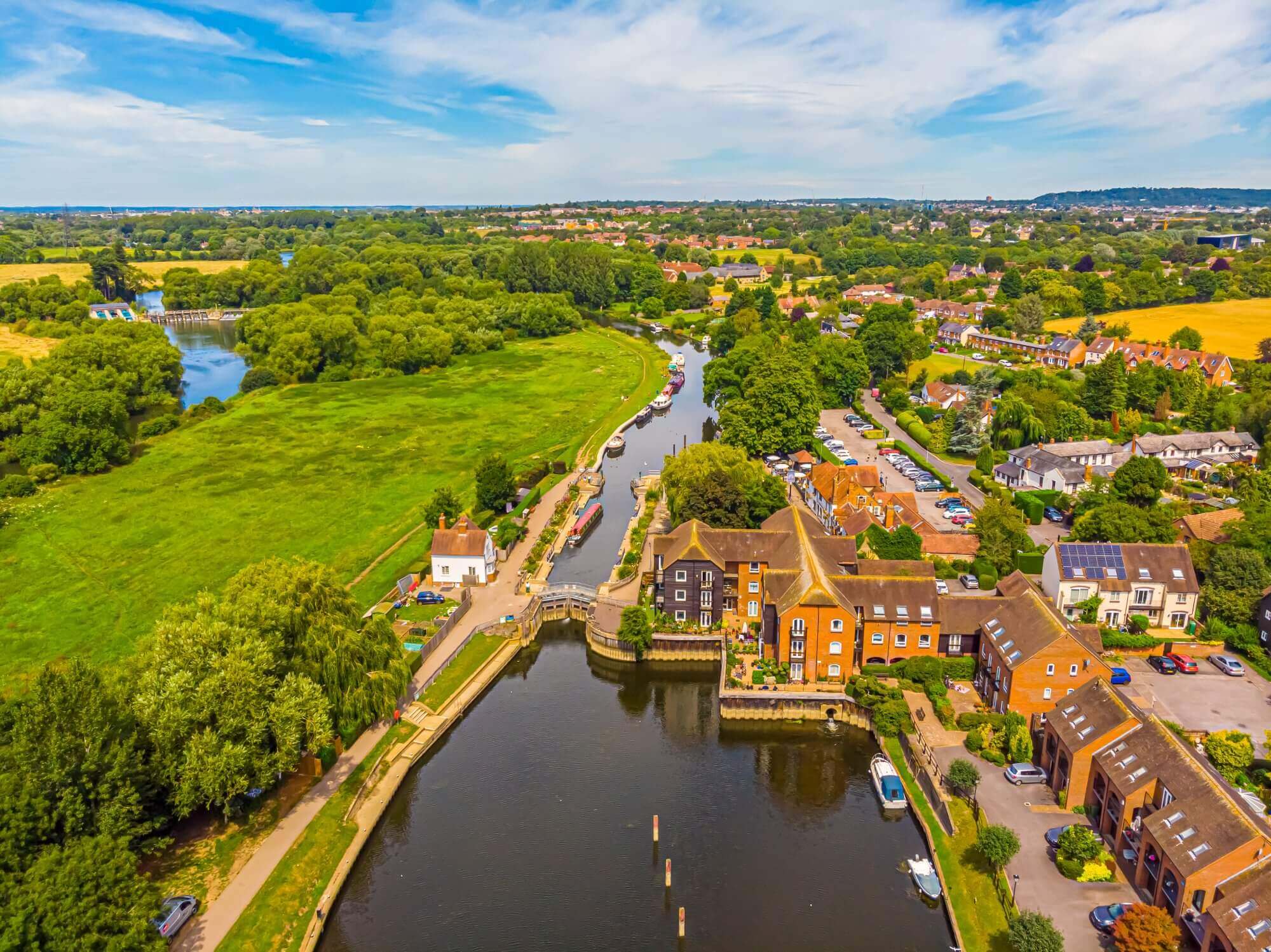 Aerial view of a picturesque town along a river, surrounded by green fields and trees under a blue sky. - Home Instead