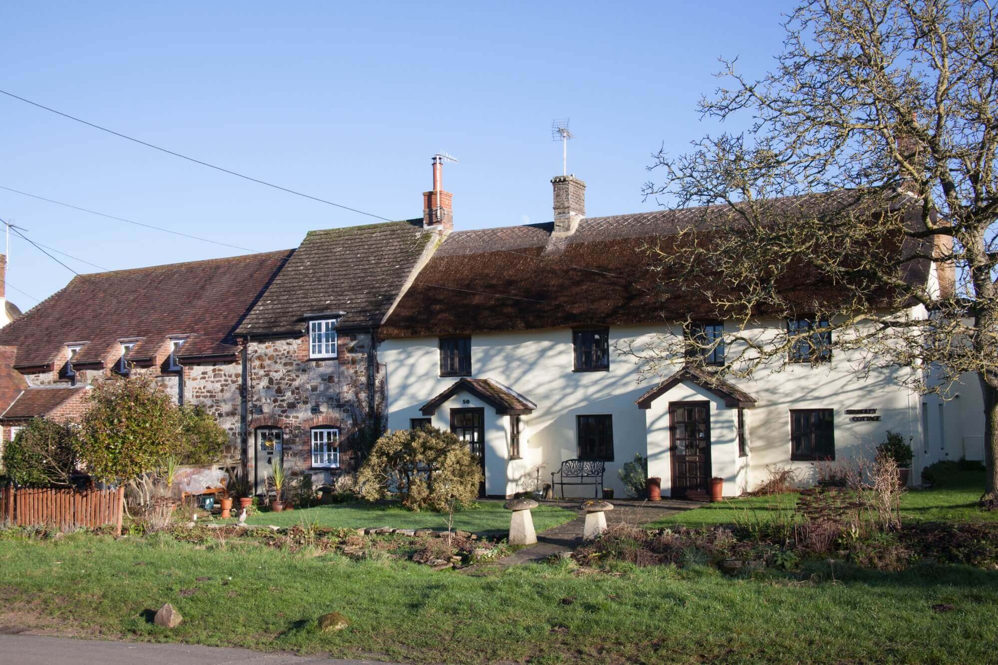 A row of quaint cottages with a garden in front, under a blue sky. - Home Instead