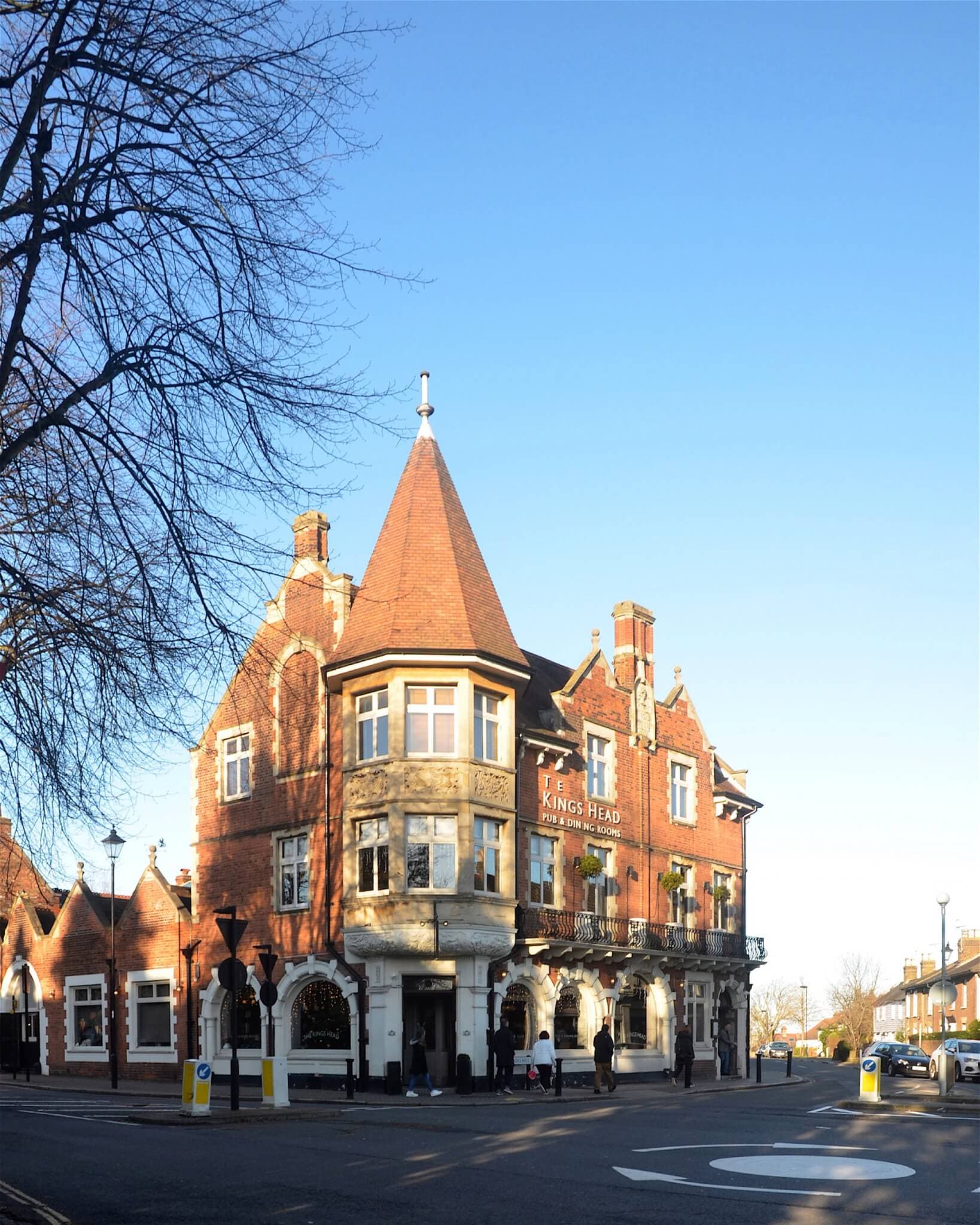 A historic brick building with a turret labeled "The King's Head" on a sunny street corner. - Home Instead