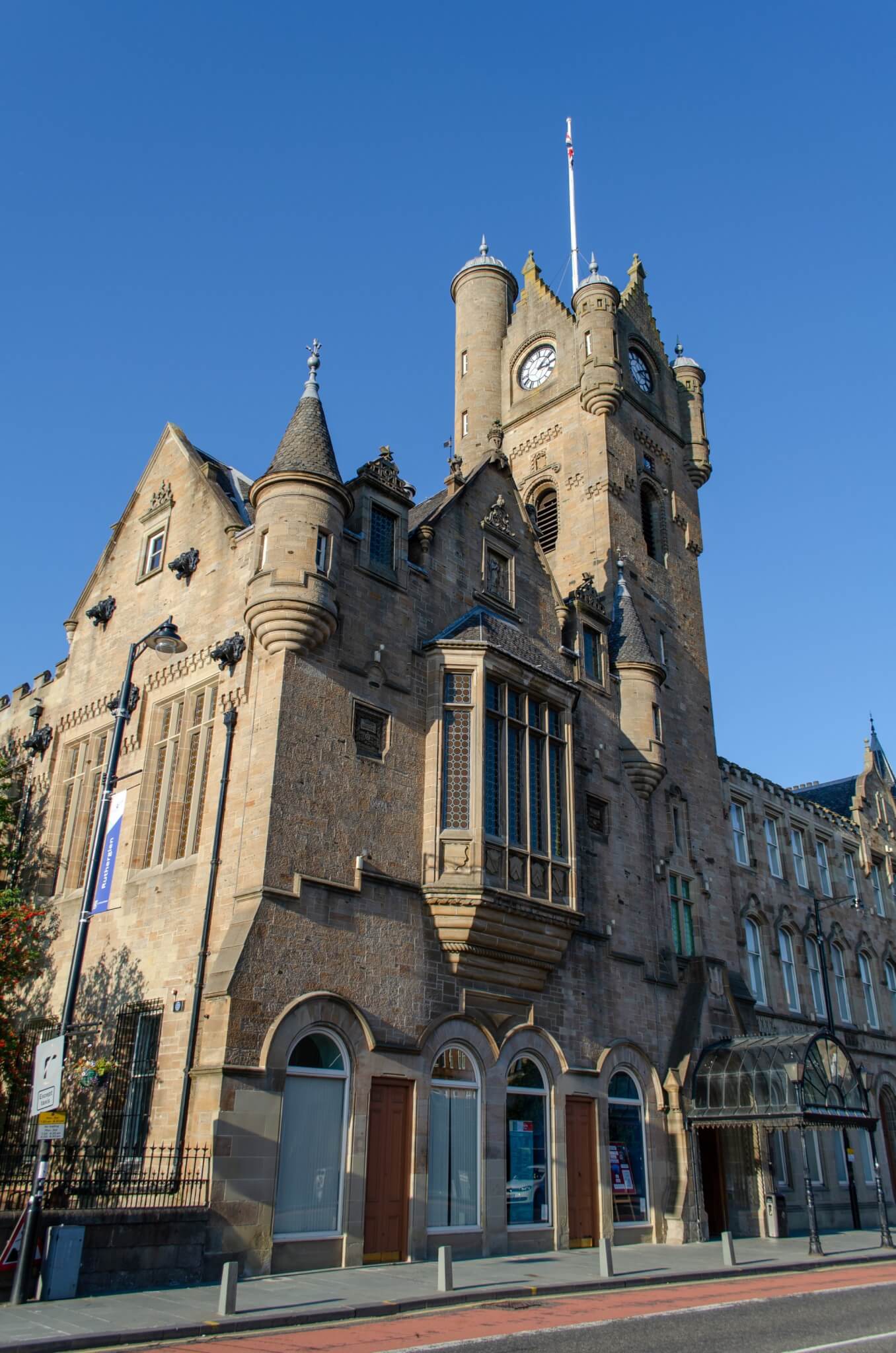 Historic stone building with a clock tower under a clear blue sky, featuring arched windows and decorative turrets. - Home Instead
