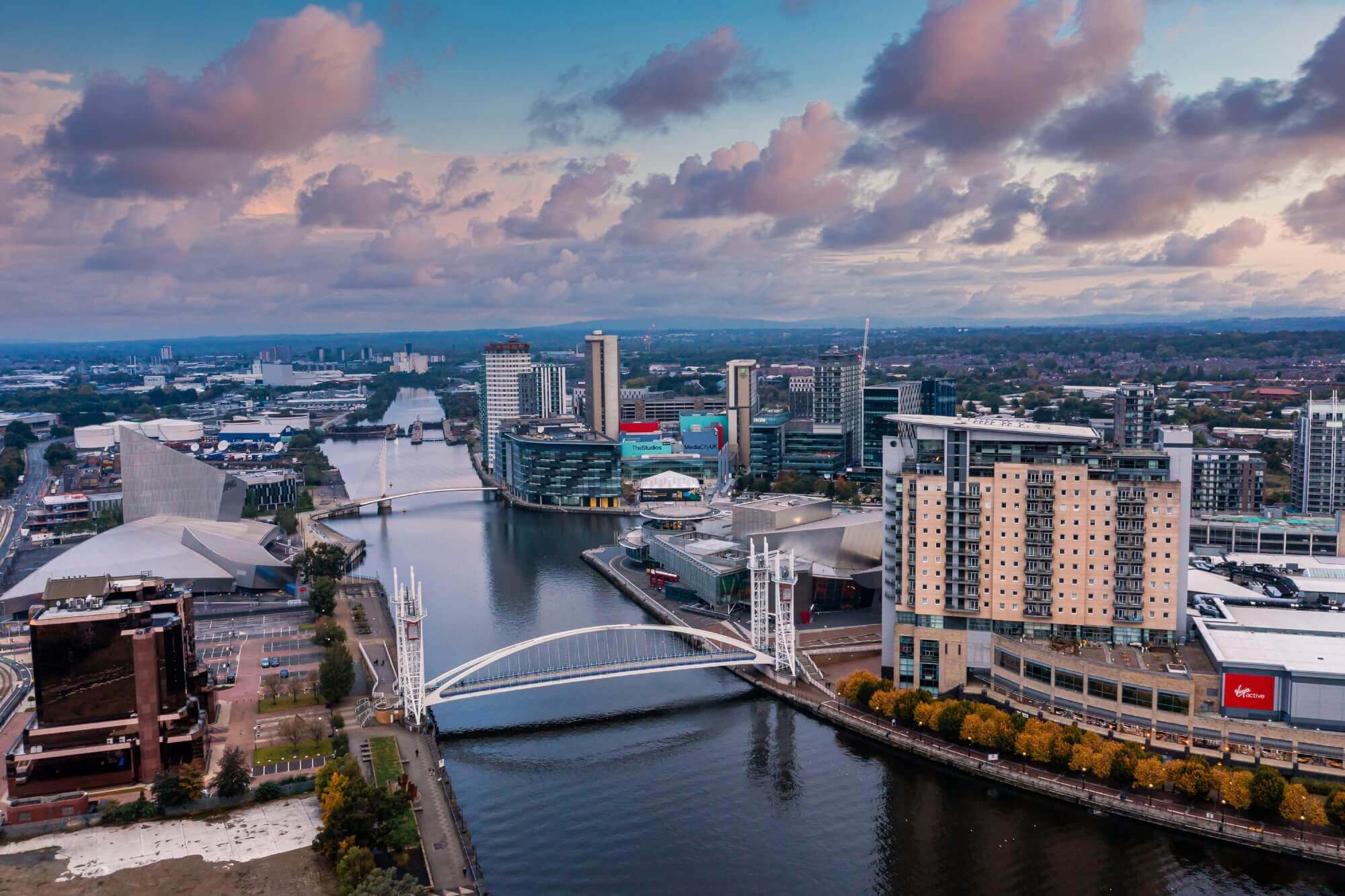 Aerial view of a cityscape with a river, bridge, high-rise buildings, and a partly cloudy sky at dusk. - Home Instead