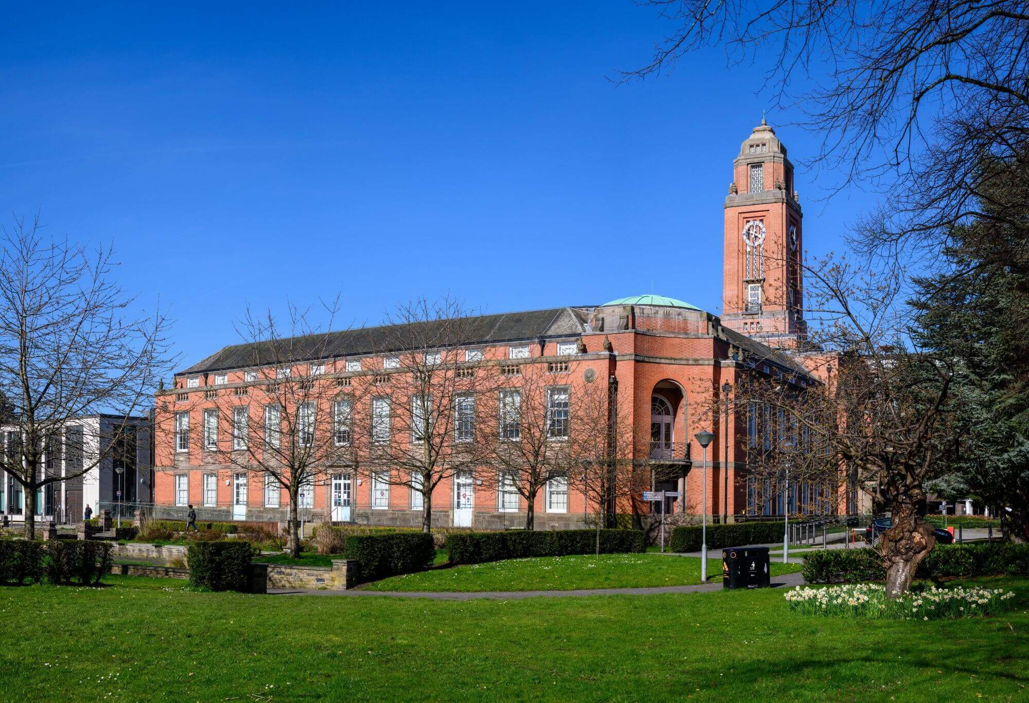 A large brick building with a clock tower surrounded by trees and greenery under a clear blue sky. - Home Instead