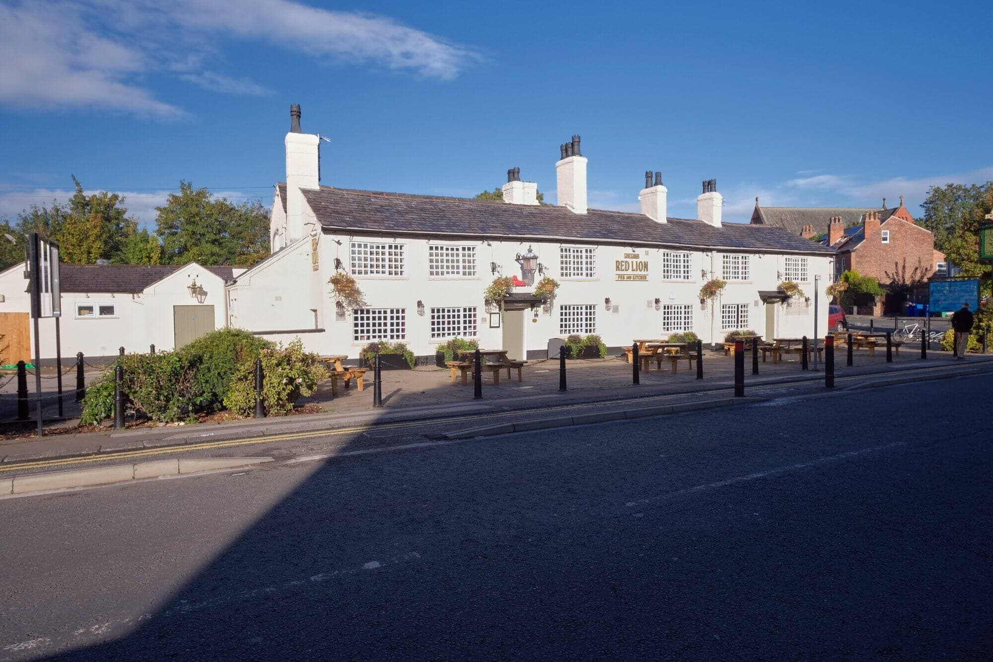A white inn with outdoor seating and hanging plants along the walls on a sunny day. - Home Instead