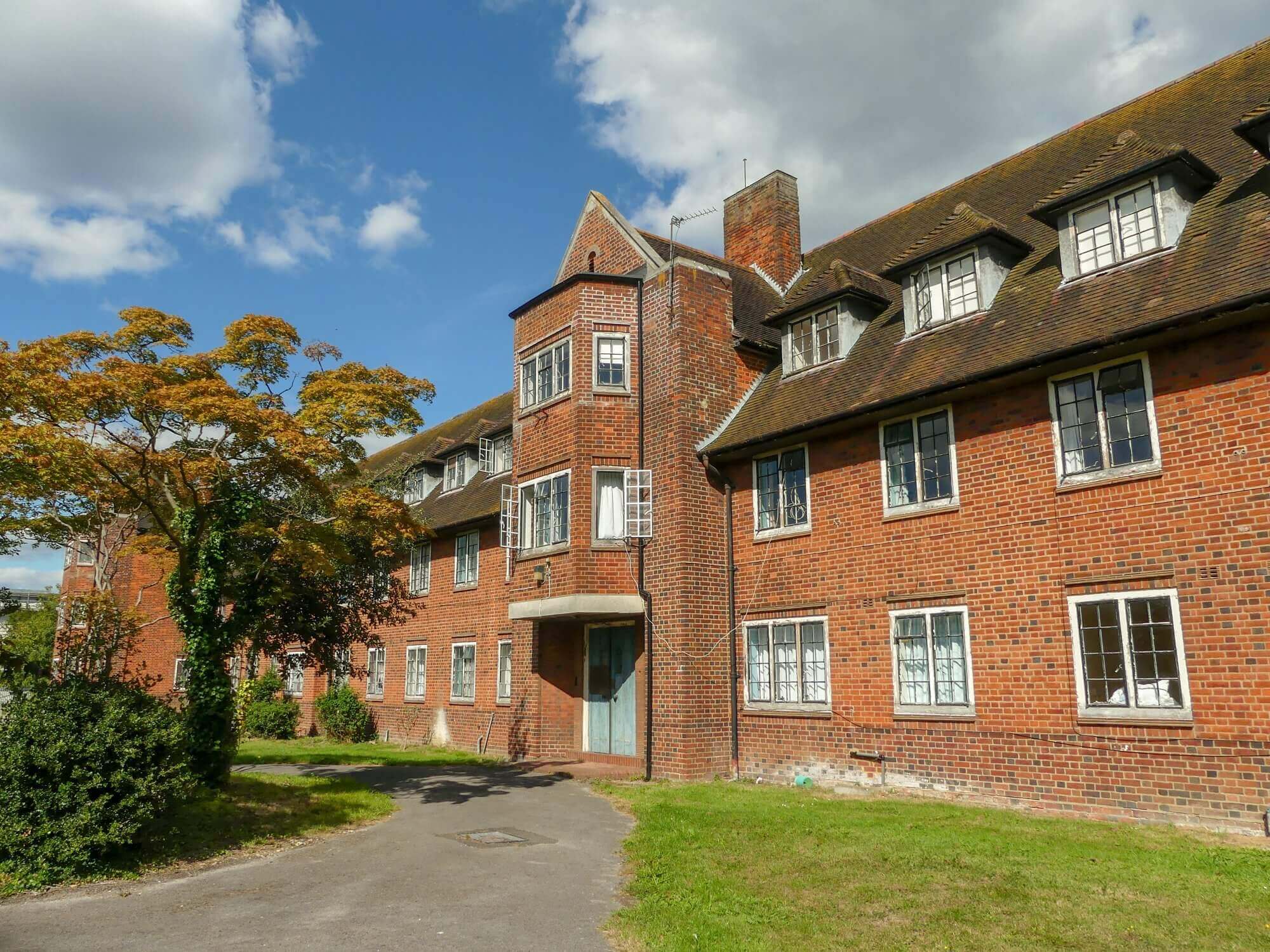 A brick building with dormer windows, trees, and a cloudy sky backdrop. - Home Instead Southampton