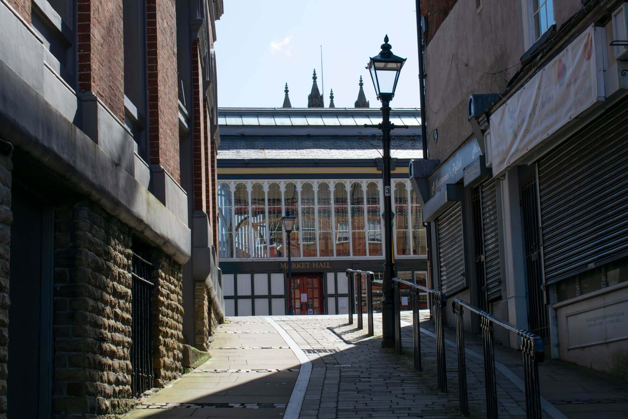 Narrow alleyway leading to a glass-fronted market hall with vintage street lamps and closed shop shutters. - Home Instead