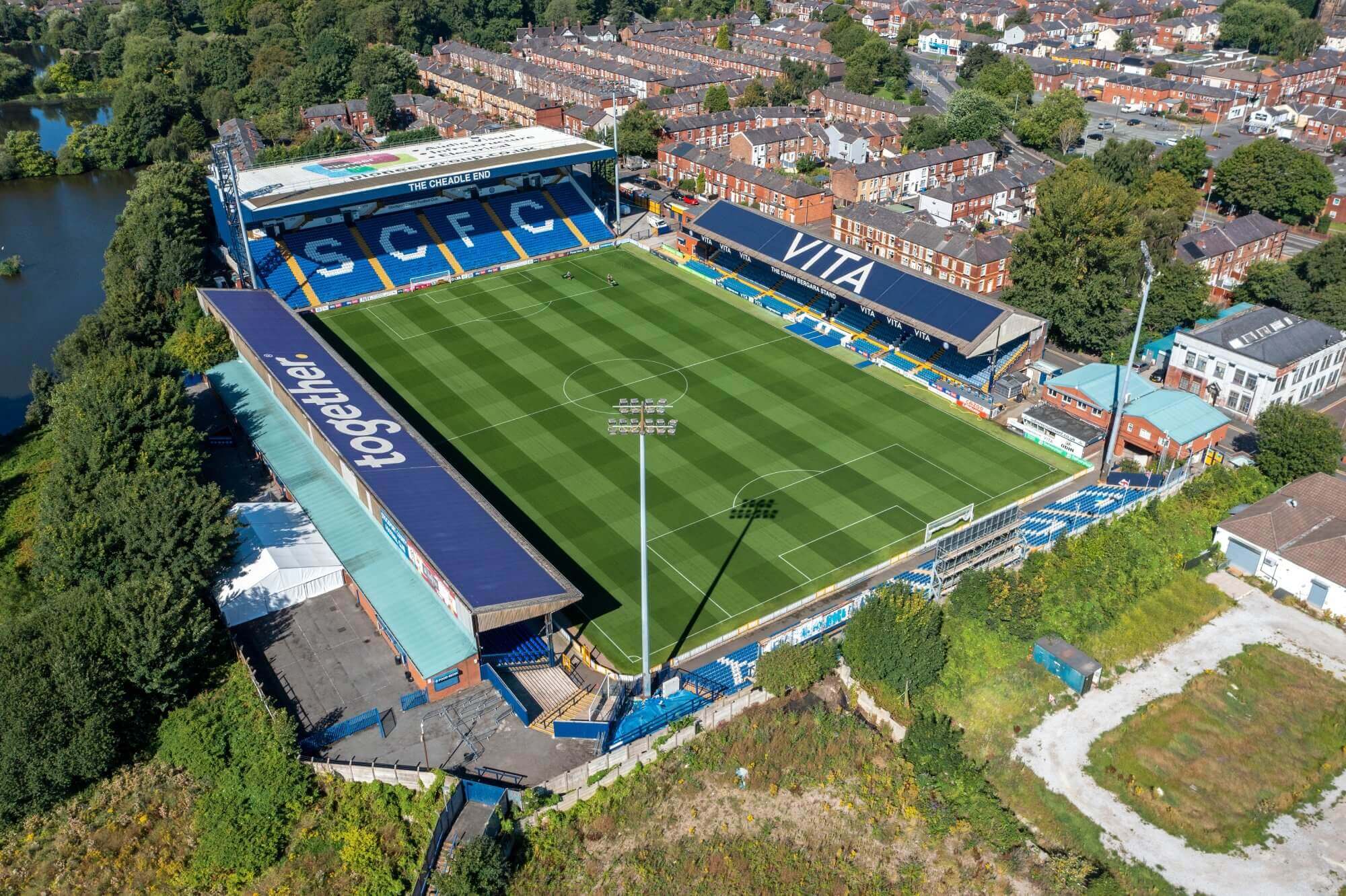 Aerial view of a soccer stadium surrounded by trees and residential buildings on a sunny day, with "SCFC" in the stands. - Home Instead