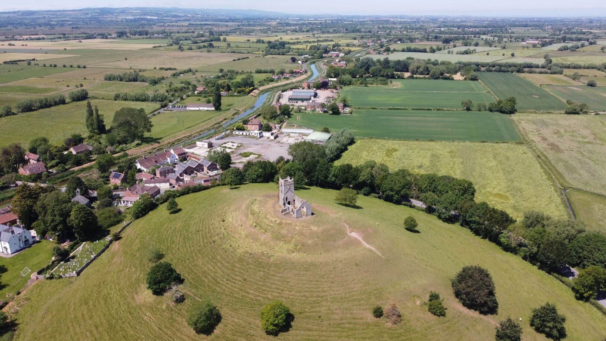 Aerial view of a rural landscape with a historic stone building on a hill surrounded by fields and homes. - Home Instead