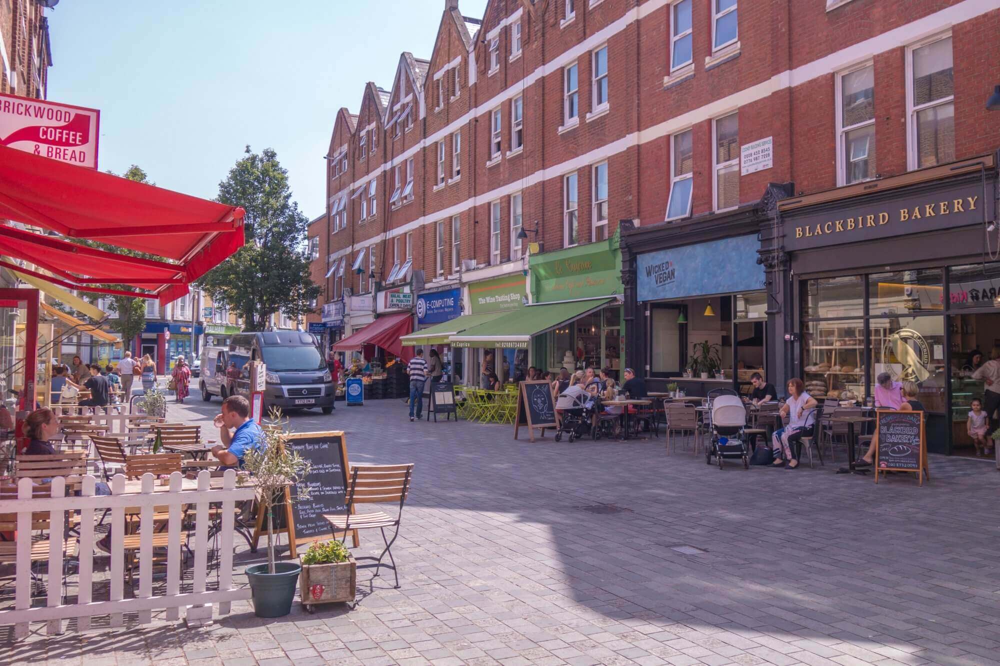 A street with outdoor cafés, people dining, red and green shop awnings, and buildings with brick facades. - Home Instead