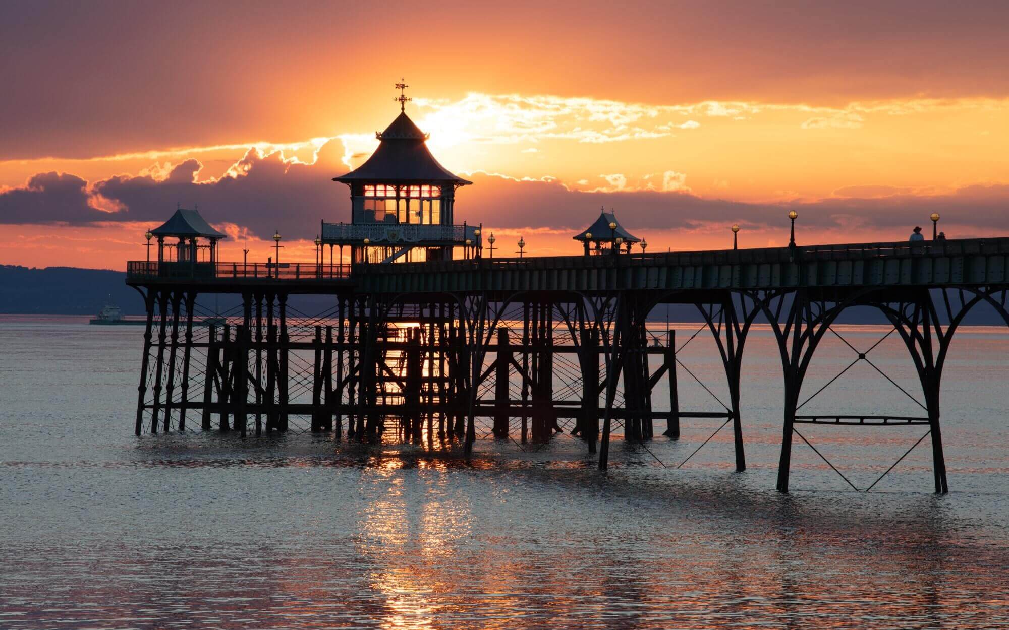 Sunset behind a pier with Victorian-style pavilions, reflecting on calm water. - Home Instead
