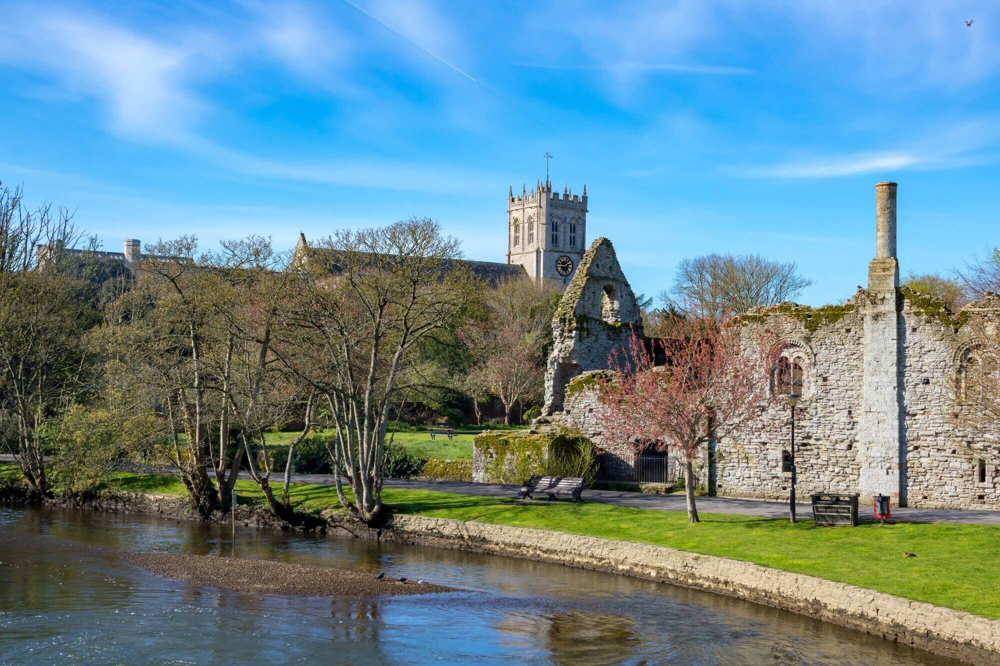 Riverside view of historic buildings and ruins under a blue sky with a tall tower and leafless trees in early spring. - Home Instead