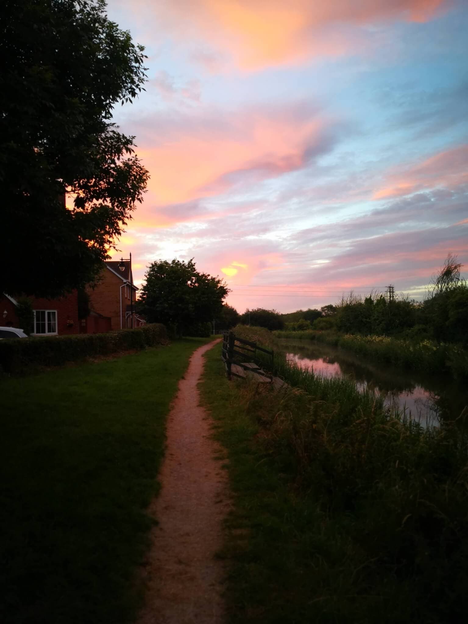 A serene path beside a canal at sunset, with a house on the left and a vibrant pink and blue sky above. - Home Instead