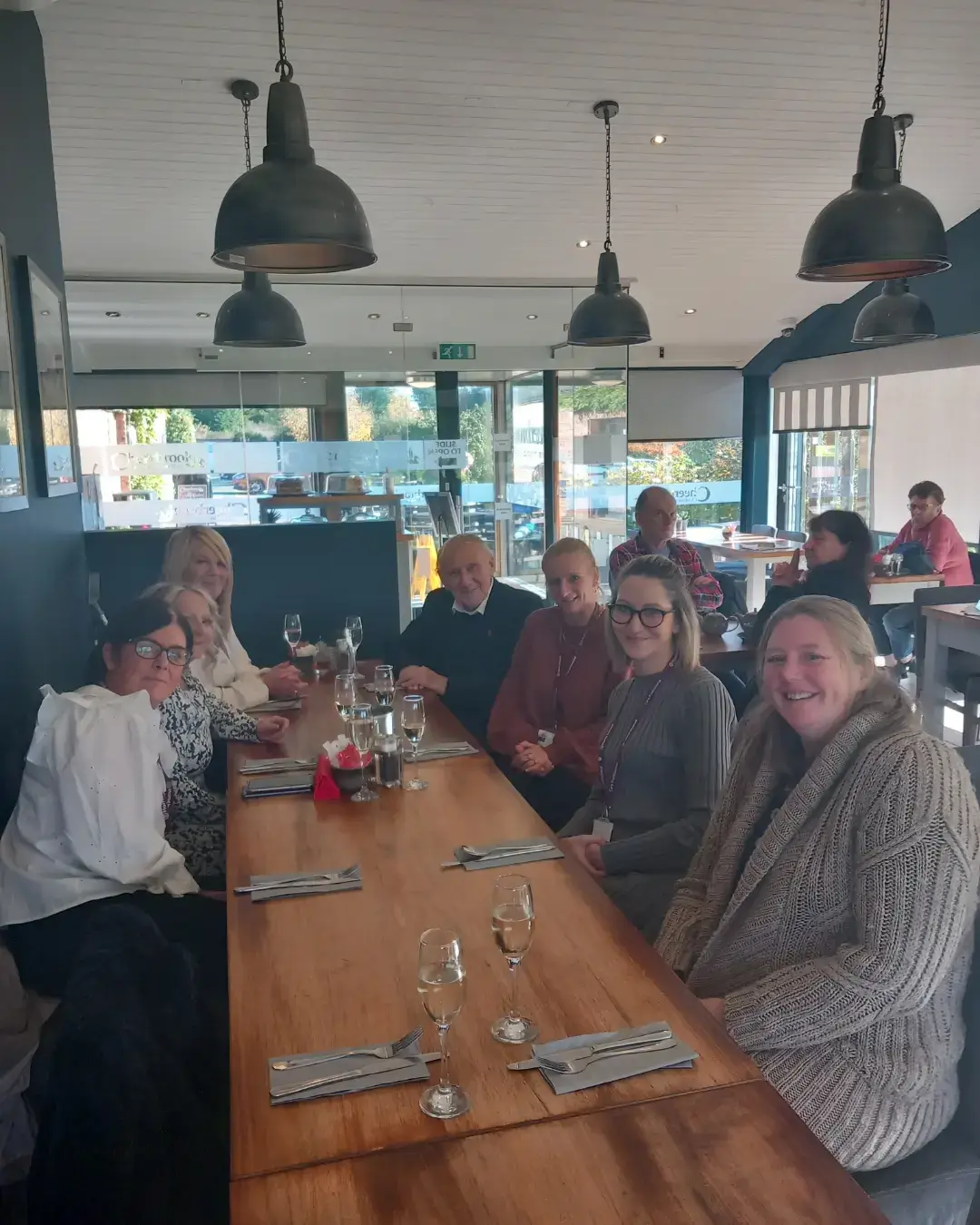 A group of six people sitting at a long table with wine glasses in a restaurant. - Home Instead