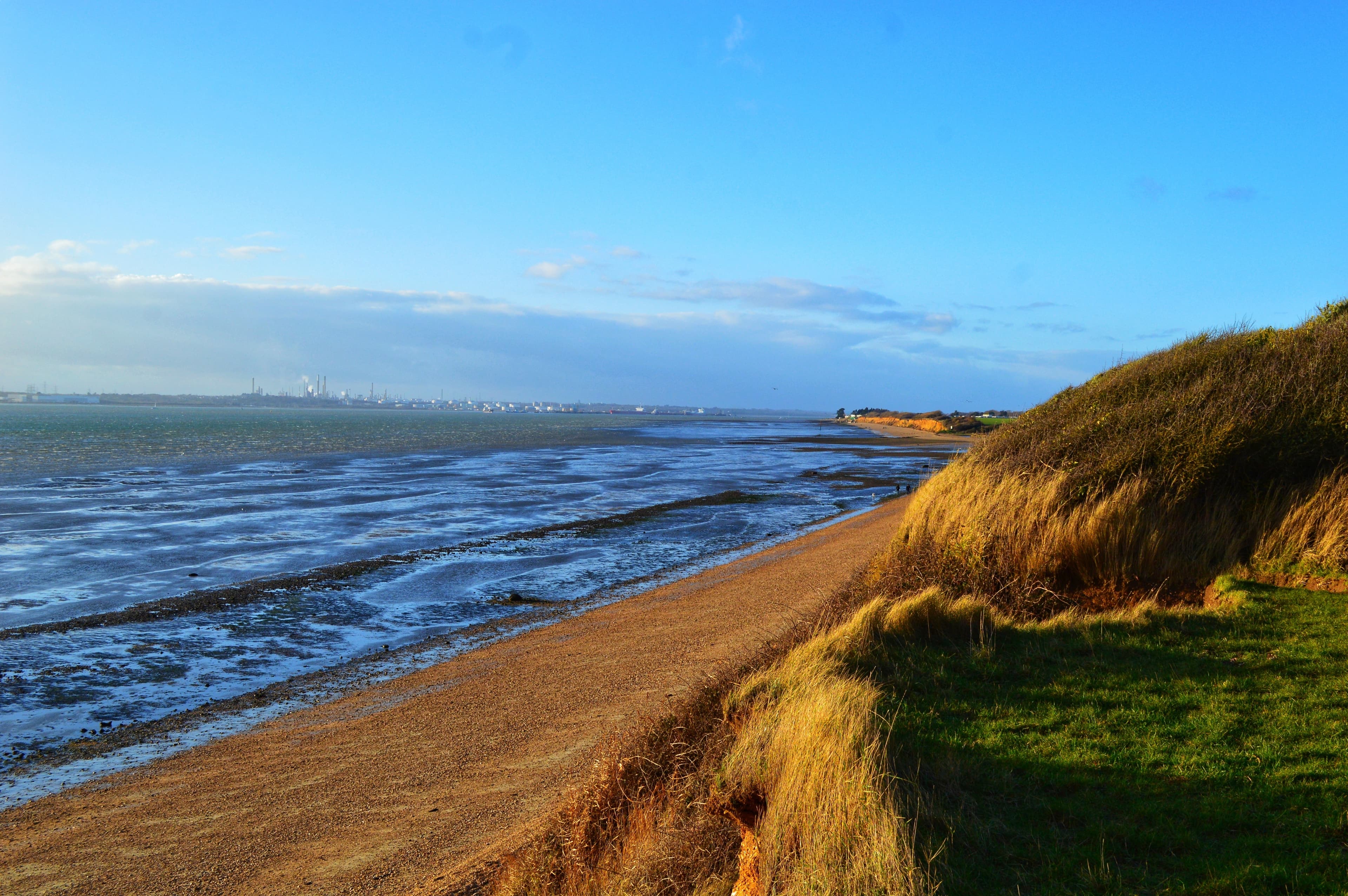 Coastal landscape with a sandy path and grassy dunes on a sunny day, overlooking the sea under a blue sky with scattered clouds. - Home Instead