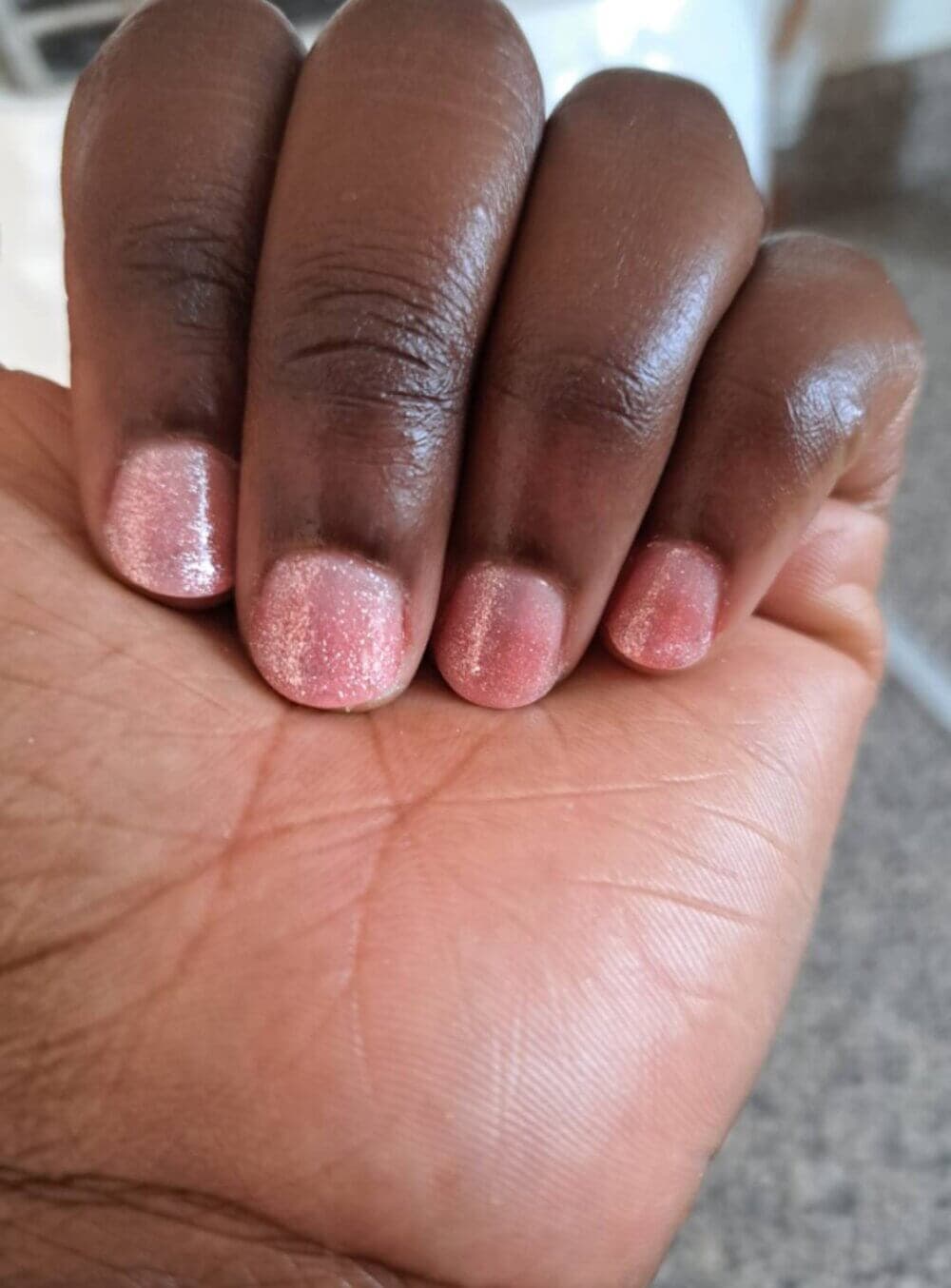 A close-up of a hand with short nails painted with sparkly pink nail polish. - Home Instead