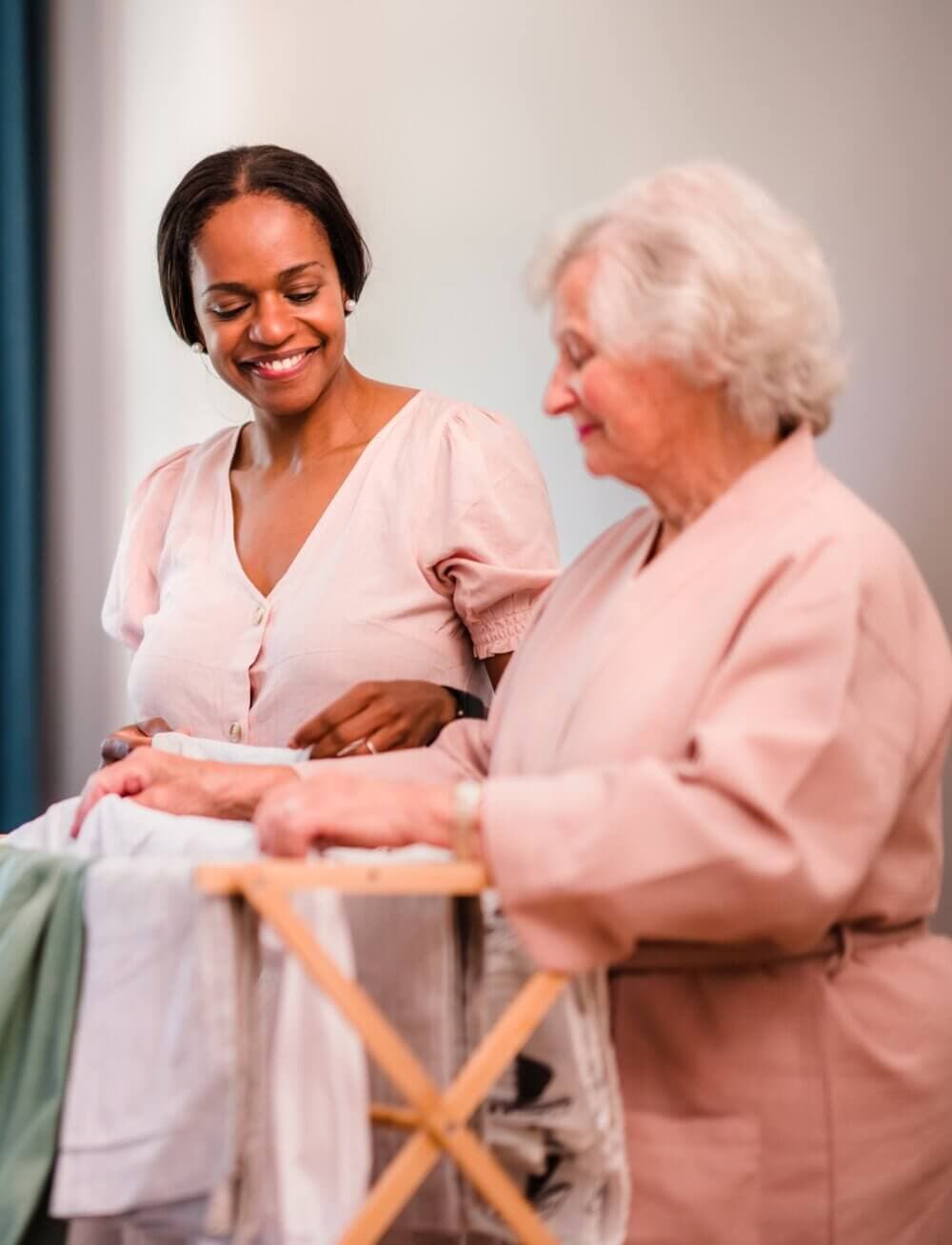 Care Professional in a purple shirt assisting an elderly man in a wheelchair in a cosy, book-filled room. - Home Instead Poole