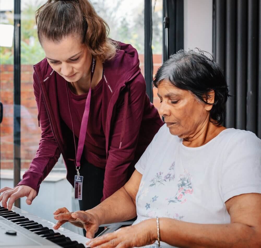 An elderly woman and a caregiver smiling and looking at a magazine together on a couch. - Home Instead