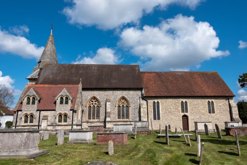 A stone church with a tall steeple, surrounded by a cemetery, under a blue sky with scattered clouds. - Home Instead