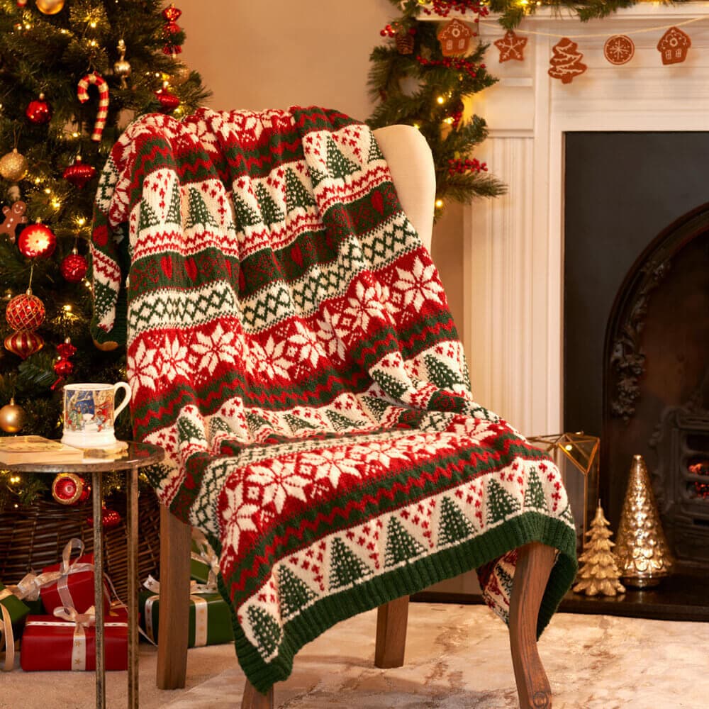 Cozy chair with a festive blanket and a mug beside a decorated Christmas tree and fireplace. - Home Instead