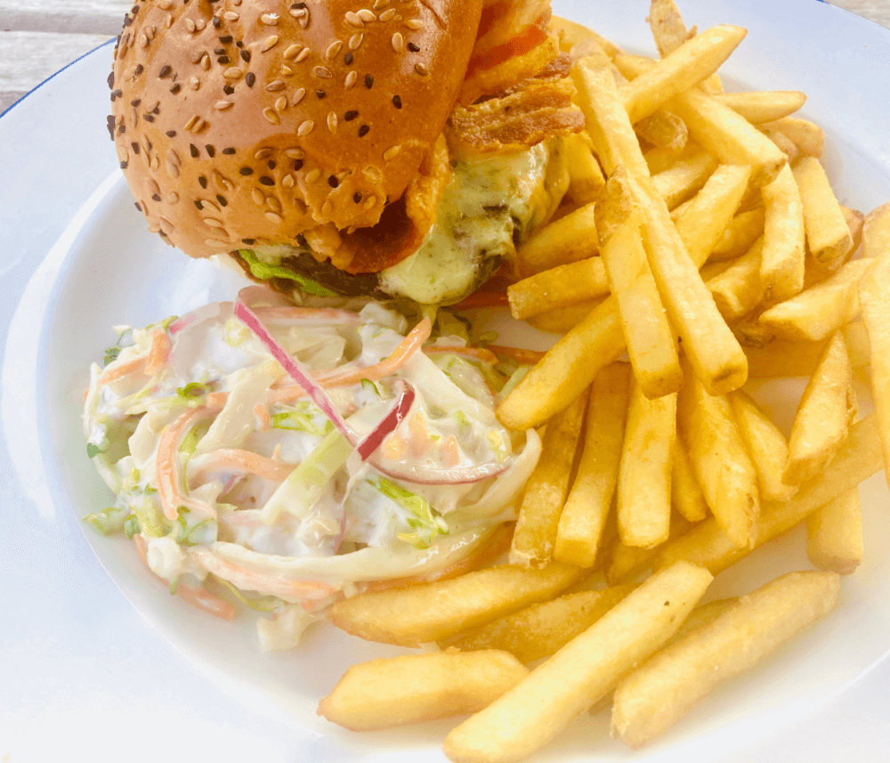 Burger with fries and coleslaw on a white plate. Topped with sesame seeds and cheese. - Home Instead