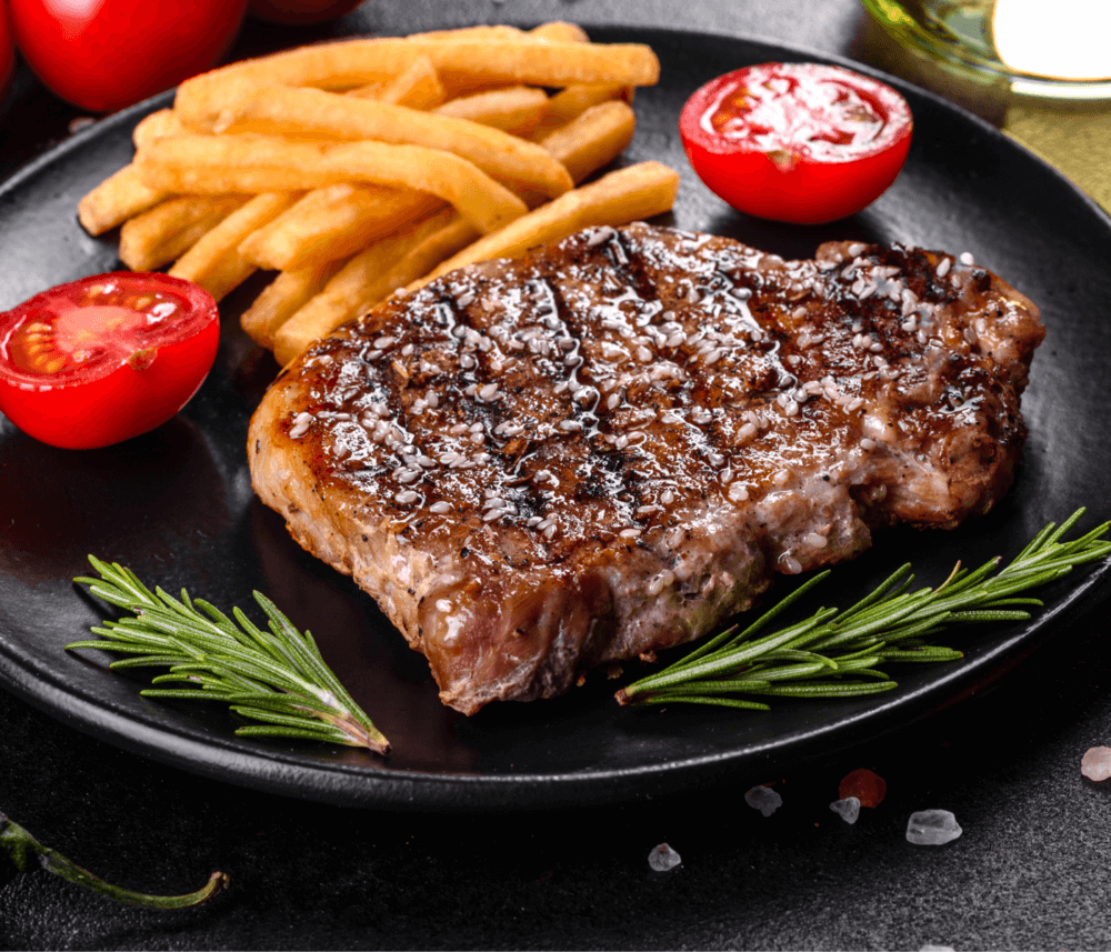 Grilled steak with French fries, cherry tomatoes, and rosemary garnished on a black plate. - Home Instead