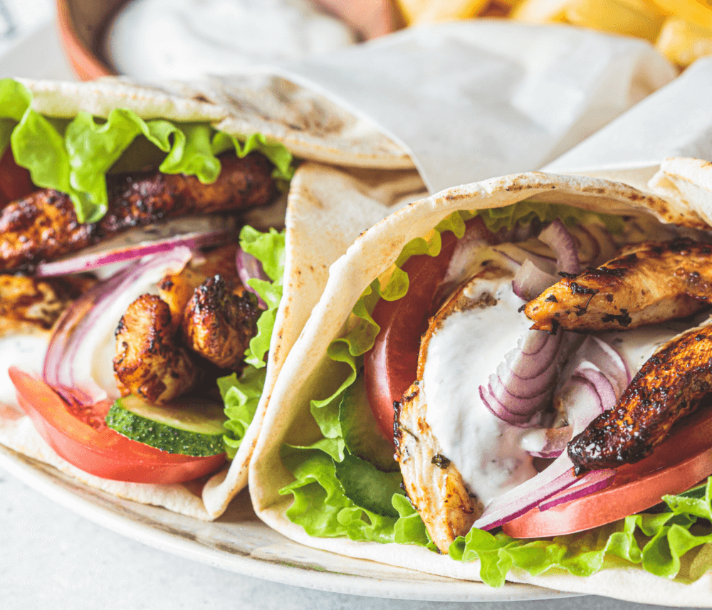 Two pita wraps filled with grilled chicken, lettuce, tomato, cucumber, red onion, and sauce. - Home Instead