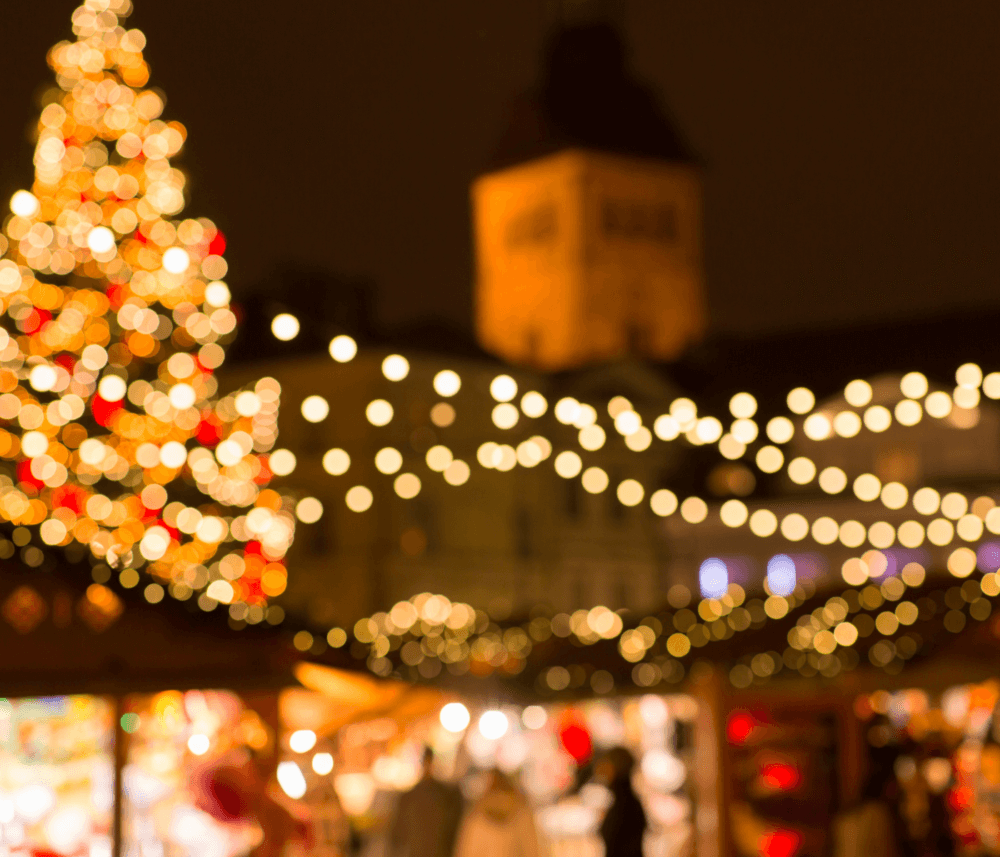 Blurred festive scene with illuminated Christmas tree and string lights, warm atmosphere, and people in the background. - Home Instead