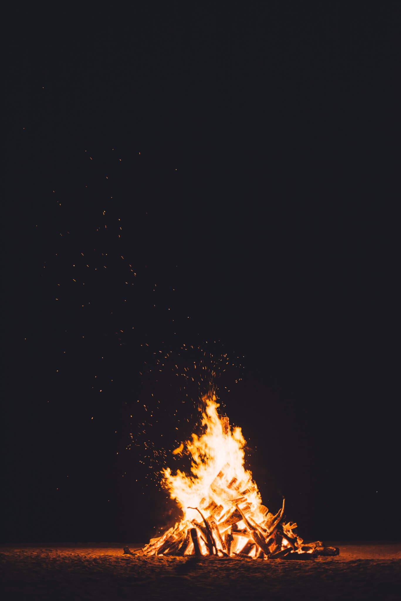 A bonfire burning brightly against a dark background, with sparks flying into the night sky. - Home Instead