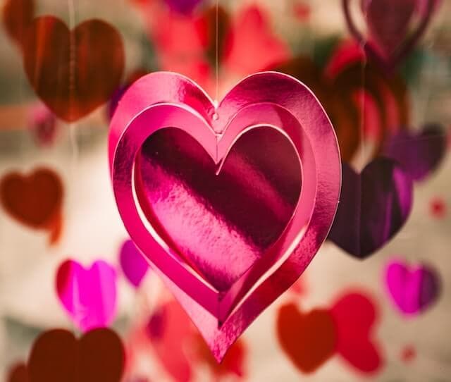 Close-up of pink and red paper hearts hanging as decorations, with a large pink heart in the center. - Home Instead