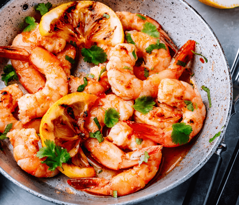 A pan of cooked shrimp garnished with cilantro and slices of caramelized lemon. - Home Instead