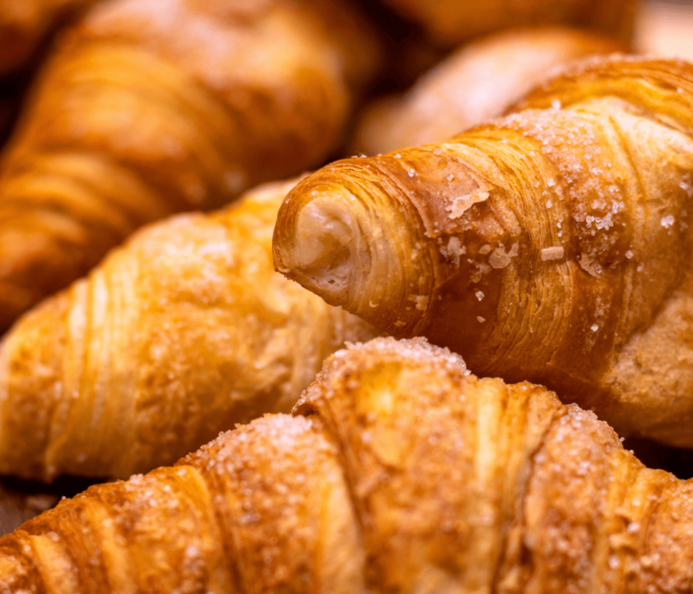 Close-up of golden, flaky croissants with sugar crystals on top. - Home Instead