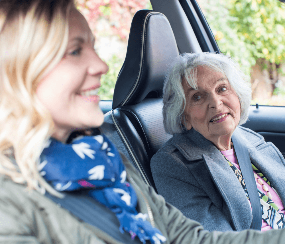 Older woman smiling in the passenger seat while younger woman drives a car. - Home Instead